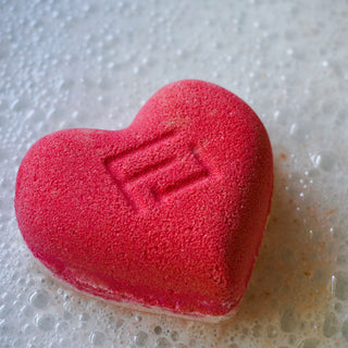 a red and white, heart - shaped bath bomb on a background of bubbles.